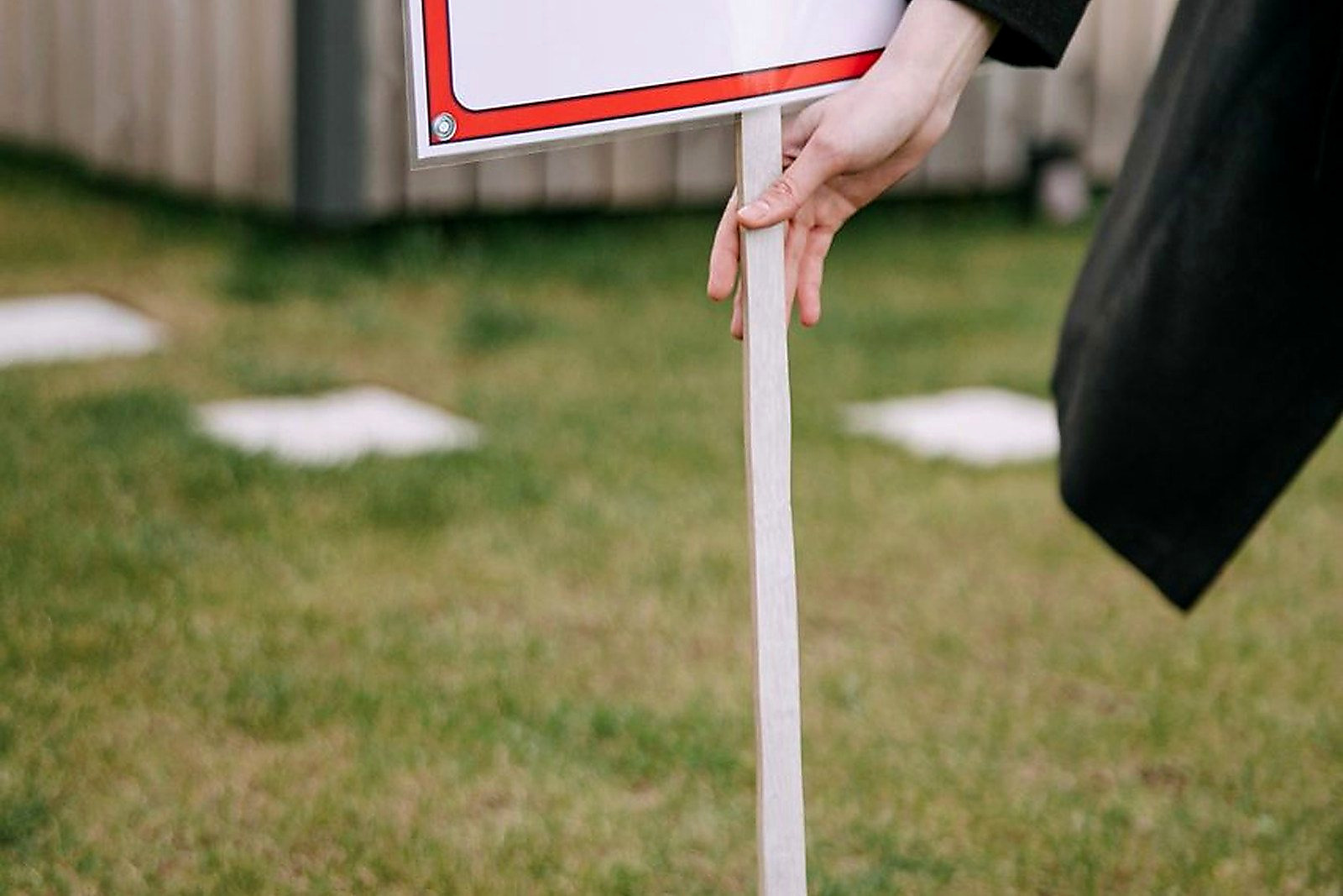 Free Close-up of a red 'House for Rent' sign on a grassy lawn, hand holding pole. Stock Photo